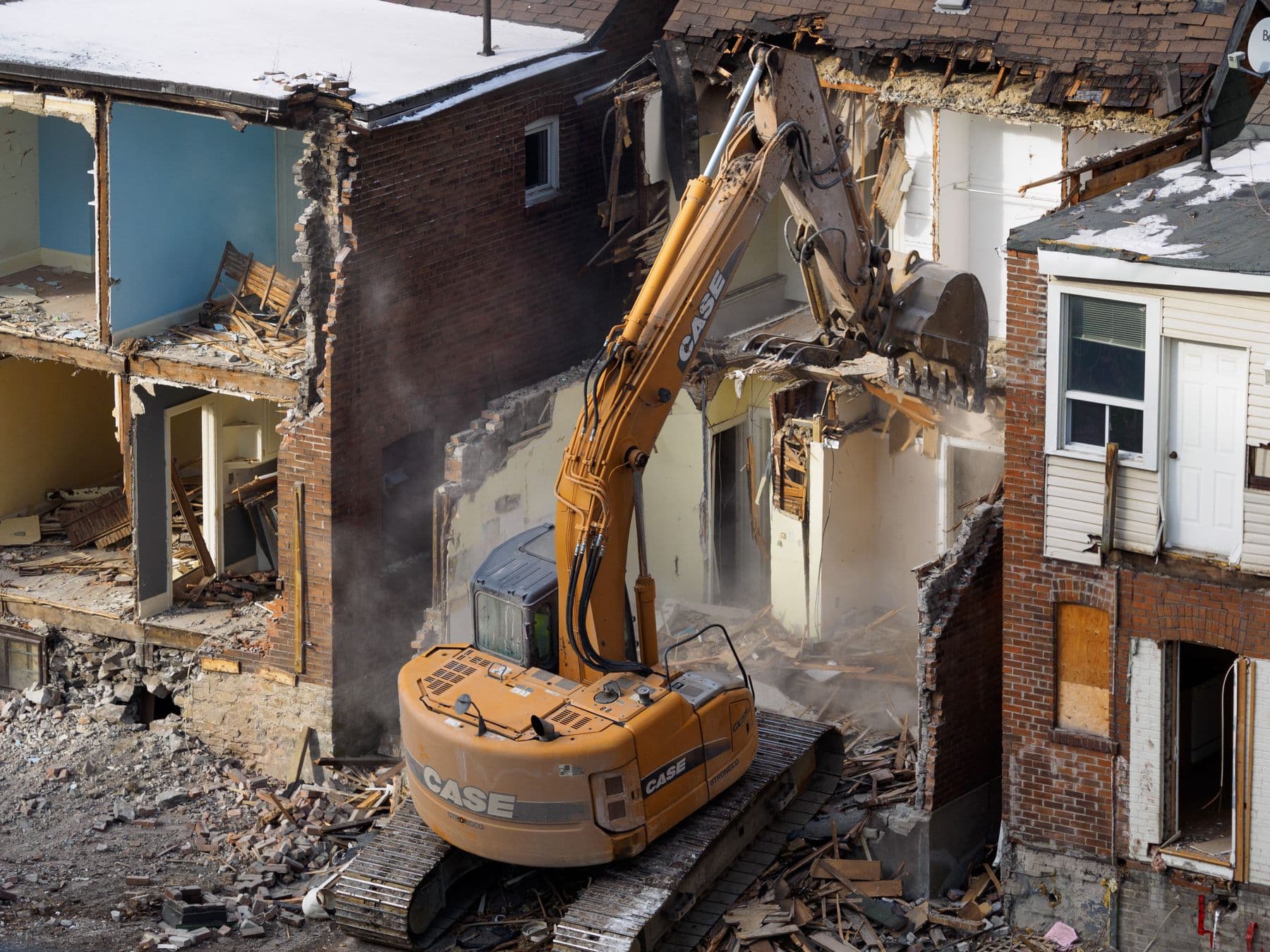 A yellow excavator working inside a partly demolished brick row building, with open rooms visible on each floor.