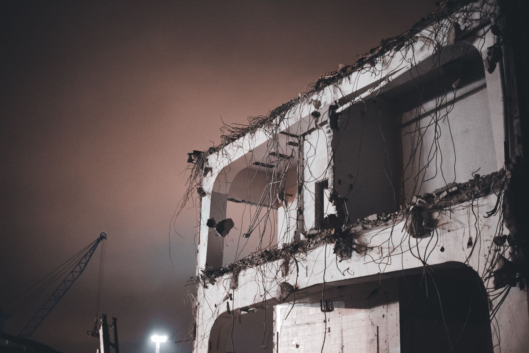 The concrete frame of a building half torn down at dusk, with wires and rebar hanging from the slabs.