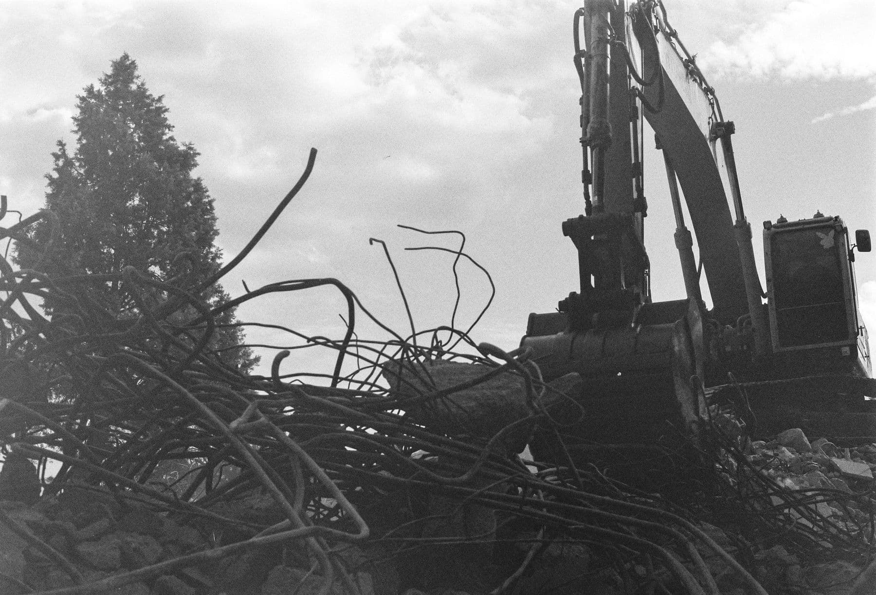 A black-and-white photo of an excavator above a tangled pile of steel rebar.